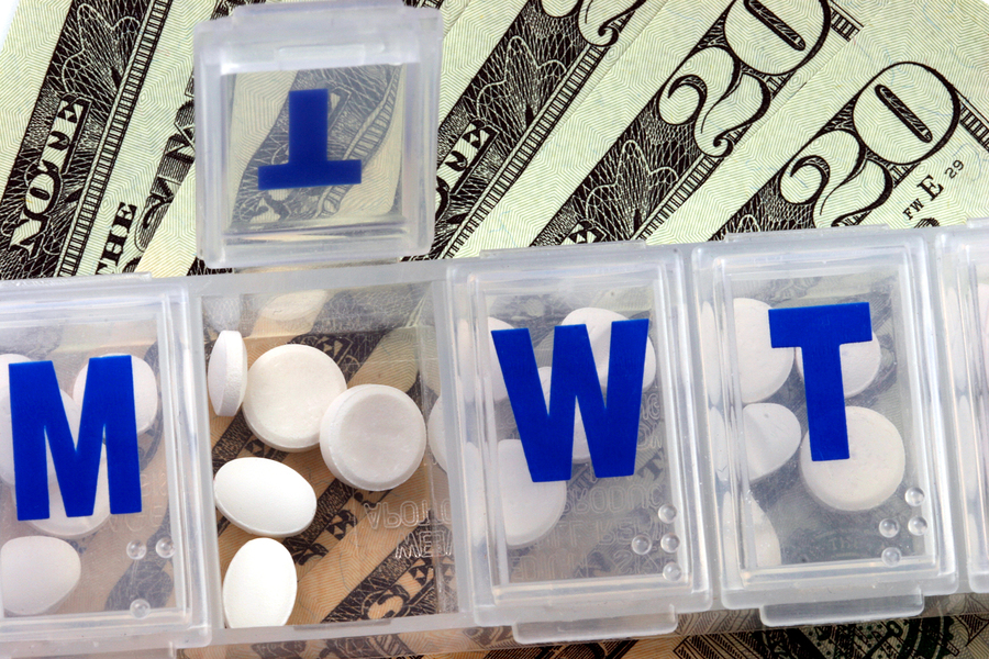close up of an open medicine container over a stack of bills.